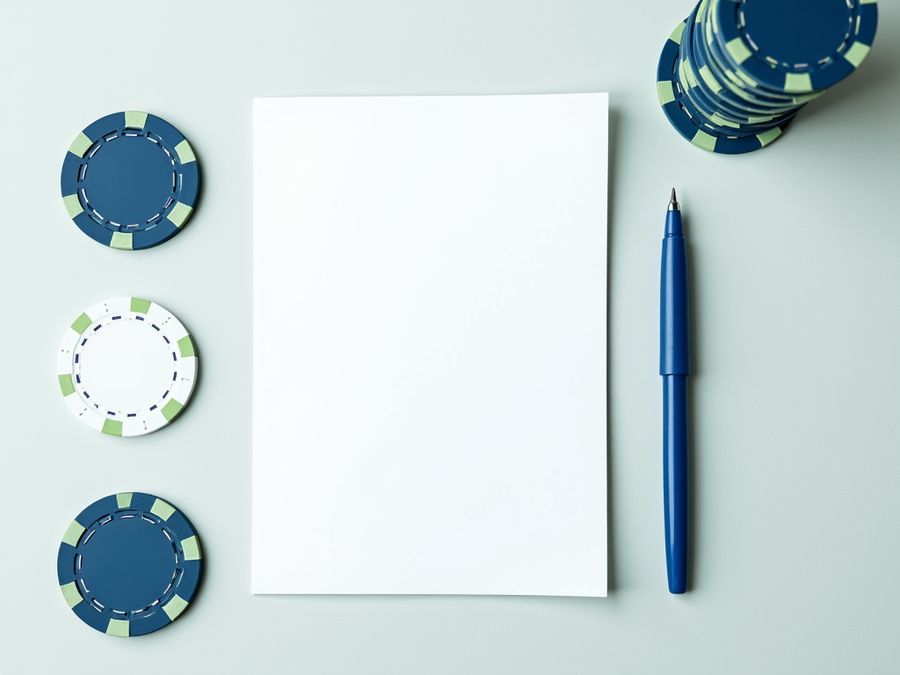 Taitettu tyhjä paperi, kynä ja pino pelimerkkejä vaalealla huovalla